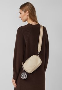 Borsa a tracolla beige in pelle texturizzata con una pochette rotonda staccabile a stampa leopardata. Presenta una larga tracolla regolabile e hardware metallico.