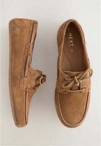 Paire de mocassins en daim marron avec lacets en cuir et semelles en caoutchouc, montrée de dessus et de côté sur fond blanc.