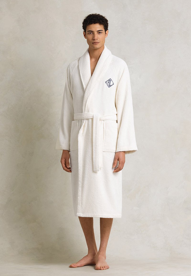 Accappatoio bianco in spugna con colletto a scialle, cintura da annodare e tasche laterali. Presenta un logo ricamato sul petto. Morbido e strutturato.