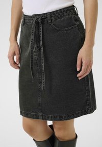 Jupe en denim noir avec une coupe décontractée, dotée d'une taille ceinturée, de poches latérales et d'un ourlet qui tombe juste au-dessus du genou.