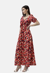 Maxikleid mit floralem Muster in Rot, Creme und Blau. Hat kurze puffige Ärmel und eine taillierte Taille. Wird mit weißen Absatzsandalen getragen.