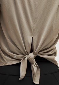 Khaki short-sleeve top featuring a knot-tied design at the back, with a small slit above the knot. Fabric appears soft and lightweight.