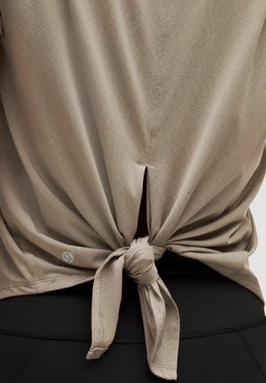 Khaki short-sleeve top featuring a knot-tied design at the back, with a small slit above the knot. Fabric appears soft and lightweight.
