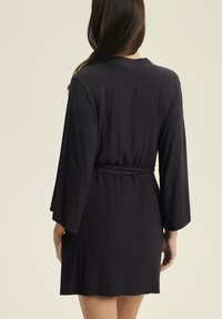 Czarna, strukturalna szata z długimi, szerokimi rękawami i paskiem w talii. Projekt charakteryzuje się materiałem w prążki oraz długością do połowy ud.