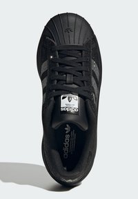 Black athletic shoe with a textured upper, rubber toe cap, and three white stripes on the side. Features black laces and logo on the tongue.