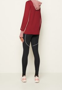 Bordeauxroter Langarm-Hoodie mit einer pinken Kapuze, kombiniert mit schwarzen Leggings mit weißen Akzenten. Leichter Stoff mit sportlichem Design.