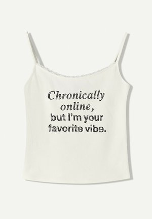 Camisole blanche avec des bretelles réglables, présentant une bordure en dentelle et un texte imprimé en noir : "Chroniquement en ligne, mais je suis ta vibe préférée."