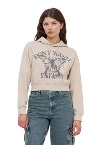 Skórzana beżowa bluza z kapturem z przodu z grafiką motyla i napisem. Posiada sznurek w kapturze i ściągacze na mankietach. Nosi się ją na wysokich spodniach dżinsowych.