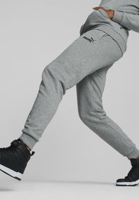 Pantalons de jogging en coton gris avec une coupe slim, ornés d'un logo Puma noir et de poignets côtelés aux chevilles, accompagnés de baskets montantes noires.