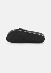 Scarpa nera slip-on con suola in gomma testurizzata e bordo bianco a contrasto. Presenta una silhouette piatta e un design minimalista.