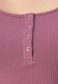 Nærbilde av ribbet mauve stoff med en vertikal rad av fire sølvknapper, delvis åpnet.