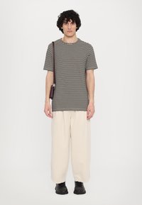 Tricou striped alb-negru, pantaloni relaxați bej, pantofi negri și o geantă întunecată de umăr. Linii simple și design curat.