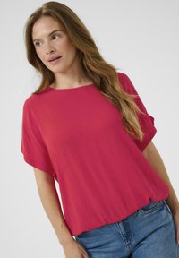 T-shirt à manches courtes en tissu rose vif, avec une coupe décontractée et un col rond simple, associé à un jean en denim bleu.
