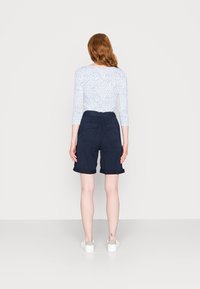 Marineblauwe shorts met opgerolde manchetten, elastische tailleband en achterzakken, gecombineerd met een witte lange mouwtop met een stippenpatroon.