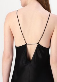 Sorte satindress med tynne stropper og dyp V-rygg. Har en elegant, glatt tekstur og minimalisk design med subtile knyte detaljer.