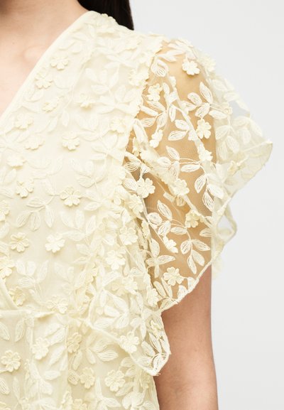Ανοιχτόκίτρινο μπλουζάκι με κεντήματα με λουλούδια, διαφανή μανίκια με βολάν και απαλό υφασμάτινο ύφασμα με ανάγλυφες λεπτομέρειες.