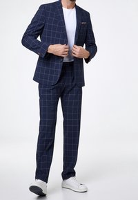 Navy checked suit featuring a tailored blazer and matching trousers. Material: smooth fabric. Accented with white grid lines and a pocket square.