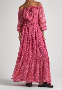 Pink off-the-shoulder maxi dress with gathered waist, sheer long sleeves, and diamond-patterned texture. Ruffled hem. Worn with black sandals.