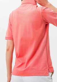Korálový polo triko s krátkými rukávy, límcem a bočními rozparky. Hladká textura a jednoduchý design, vhodné pro volnočasové nošení.