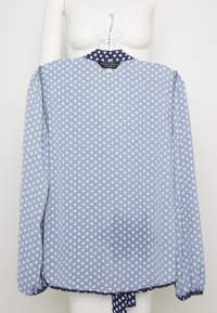 Blusa azzurra con motivo a cuori bianchi, maniche lunghe con polsini arricciati e colletto blu navy. Etichetta visibile sul retro.