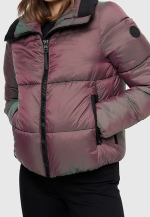 Osoba w opalizującej, fioletowej kurtce puchowej z czarnym zamkiem błyskawicznym, trzymająca ręce w zapinanych na zamek kieszeniach bocznych, na jednolitym tle.