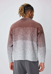 Pull en tricot avec un dégradé de couleurs rouille, gris clair et blanc. Poignets et ourlet côtelés ; texture douce avec des détails de motif dispersés.