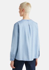 Camicia a maniche lunghe in denim azzurro chiaro, con scollatura rotonda, piega sul retro e polsini con bottone. Tessuto morbido con vestibilità ampia.