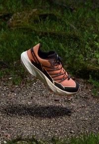 Salomon løpesko med oransje overdel, svarte detaljer og en tykk, kremfarget såle. Har et teksturert design og lissesystem.