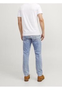 Light blue denim jeans with a straight-leg cut, paired with a plain white short-sleeve t-shirt and brown suede shoes.