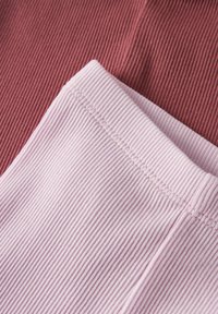 Približen posnetek zložene rebraste tkanine v svetlo roza barvi na vrhu temno roza rebraste tkanine, ki prikazuje podrobnosti šiva in teksturo.