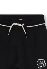 Pantaloni sportivi neri con elastico a coste in vita, cordino bianco e striscia bianca. Presentano un logo ricamato bianco sulla coscia sinistra.