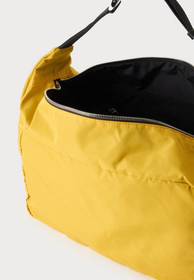 Sac à épaule jaune avec intérieur noir et fermeture éclair argentée partiellement ouverte, montrant un tissu doux et une bandoulière noire ajustable.
