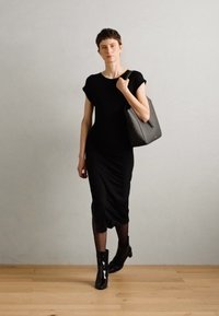 Black, fitted dress with short sleeves and a knee-length hem. Model holds a black structured handbag and wears glossy ankle boots. Smooth texture.