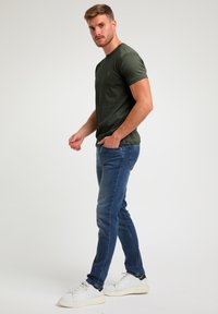 Donkergroene T-shirt met korte mouwen, gecombineerd met blauwe jeans en witte sneakers. Het T-shirt heeft een subtiele ontwerpelement op de borst.