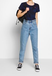 T-paita tummansinisellä kuviolla, korkeavyötäröiset vaaleat farkut ja mustat lenkkarit. Musta reppu säädettävillä kantohihnoilla.