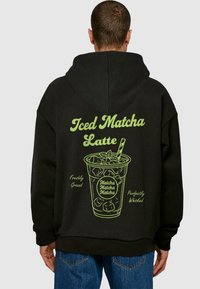 Hoodie nera con una grafica verde di un matcha latte ghiacciato con il testo "Matcha Latte Ghiacciato," "Macinato Fresco," e "Sbattuto Perfettamente."