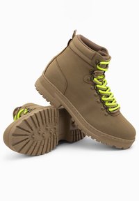 Botas altas marrones con cordones amarillos neón, suelas de goma y acabado texturizado. Presentan un tobillo reforzado y un patrón de banda de rodadura resistente.
