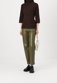 Pull à col roulé en tricot côtelé marron, manches trois-quarts, associé à un pantalon en cuir synthétique vert olive taille haute et des chaussures noires sans lacets.