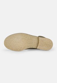 Suela de zapato con una superficie texturizada similar al caucho en color beige, con un leve tacón y un logotipo en relieve. Forma redonda con un patrón consistente.