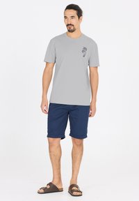 Harmaa lyhythihainen t-paita, jossa on pieni palmupuugraafi, yhdistettynä tummansinisiin shortseihin ja ruskeisiin sandaaleihin. Sujuva kangas ja rento istuvuus.