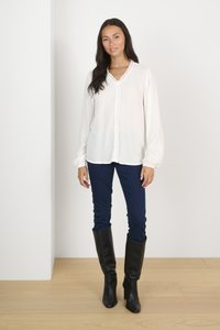White long-sleeve blouse with lace trim, paired with dark blue fitted pants and knee-high black leather boots. Simple and elegant design.