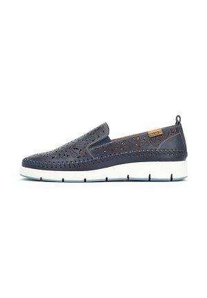 Zapato sin cordones de piel azul marino con patrón floral recortado, suela intermedia blanca y acento beige. Presenta detalles cosidos y una lengüeta trasera.