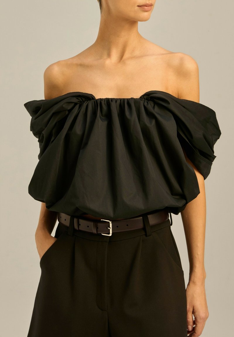 Czarna bluzka bez ramion z marszczonym dekoltem i obszerne rękawy, w połączeniu z czarnymi spodniami o wysokim stanie i brązowym paskiem.