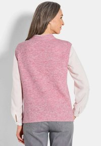 Rosa gerippter Pullover mit hohem Kragen, kombiniert mit einem langärmeligen weißen Hemd. Das Outfit hat einen Schicht-Look und eine lockere Passform.