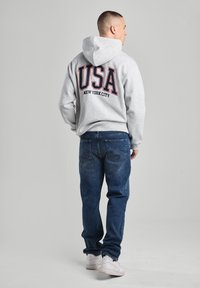 Gray hoodie with a large red "USA" and "NEW YORK CITY" print on the back, paired with blue jeans and white sneakers.