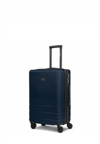 Valise rigide de couleur marine avec une surface texturée, des rayures horizontales, une poignée noire télescopique et quatre roues pivotantes pour la mobilité.