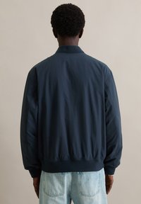 Granatowa kurtka bomberka wykonana z gładkiej tkaniny z żeberkowanym kołnierzem i mankietami, charakteryzująca się luźnym krojem oraz brakiem widocznych wzorów i zdobień.