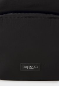 Zwarte nylon rugzak met een gladde textuur. Voorzien van een voorvak en een gestikt etiket met de tekst "Marc O'Polo EST. IN STOCKHOLM."
