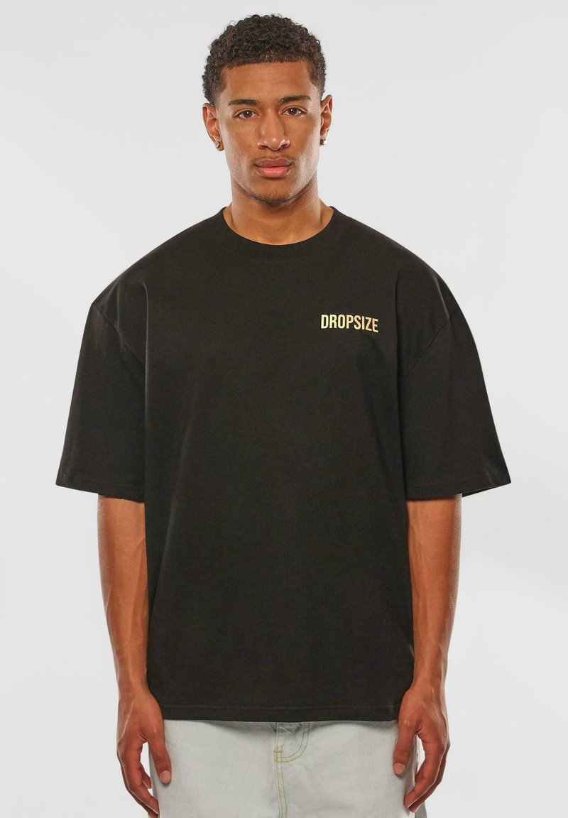 Sort oversized t-shirt lavet af bomuld, med korte ærmer og rund halsudskæring. 'DROPSIZE' er trykt i gult på venstre bryst.