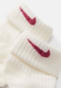 Bele sive nogavice z rebrastim vzorcem, ki na manšeti nosijo maroon Nike logo. Mehka tekstura, dolžina do sredine meč, z izrazito naglasno barvo na nevtralni podlagi.
